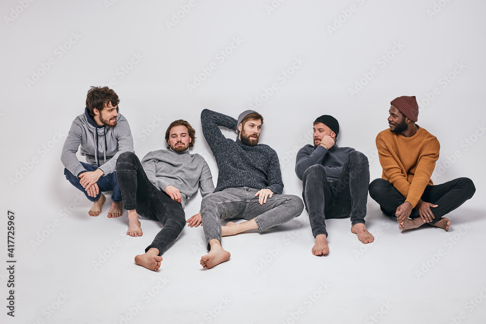 Relaxed Men Of Diverse Appearance Sit On Floor After Shooting, Have Talk, Wearing Casual Fashionable CLothes Outfit. People and fashion concept Relaxed Men Of Diverse Appearance Sit On Floor After Shooting, Have Talk, Wearing Casual Fashionable CLothes Outfit. People and fashion concept