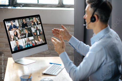 Virtuak business meeting online. Successful businessman is negotiating with multiracial business partners on a video conference using a computer while sitting at his workplace photo