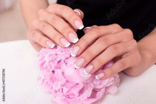 Beautiful female hands with bridal french manicure nails  pink and white gel polish  holding peonies flowers