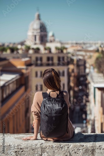 A girl enjoying the view of Rome sitting on a low wall giving the back to the camera