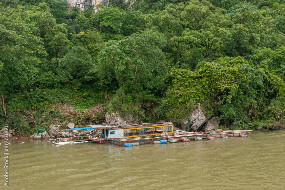 Guilin, China - May 10, 2010: Along Li River. House boat and barge docked at forested shoreline. Blues, ree, and yellow floating devices add colors.