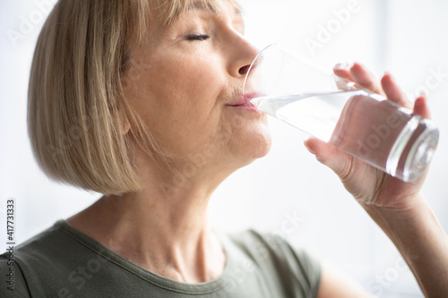 Obraz na płótnie Portrait of sporty mature woman drinking water during her workout indoors