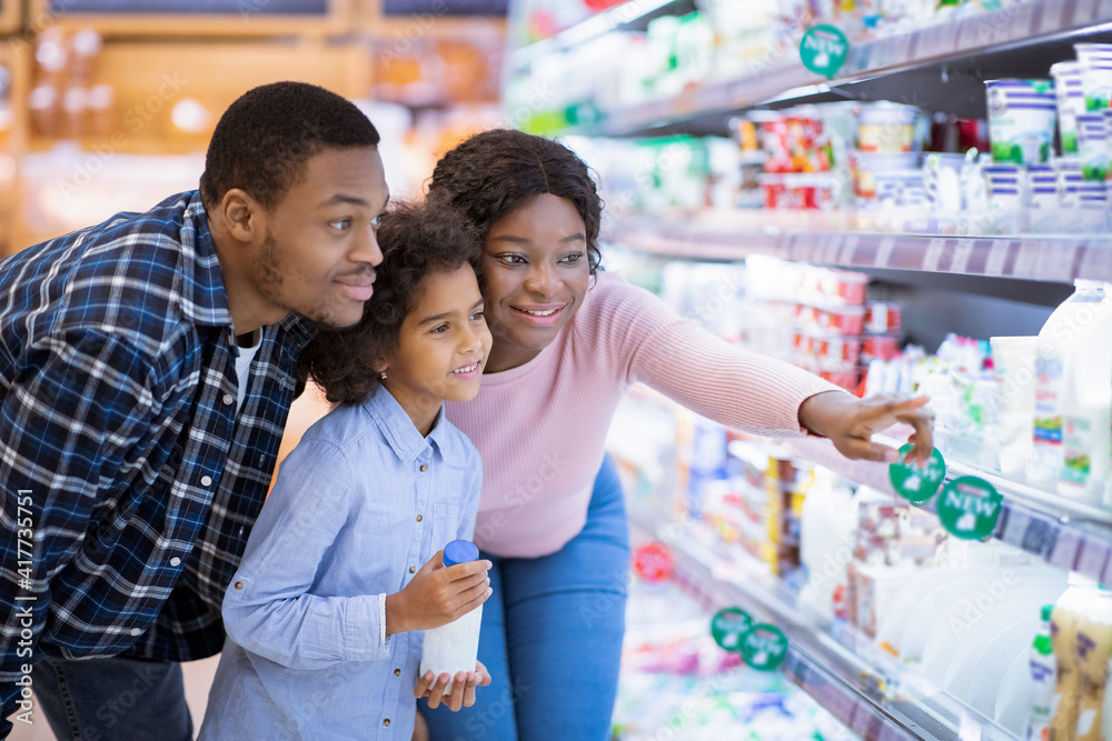 Happy African American family buying milk products at modern supermarket, empty space
