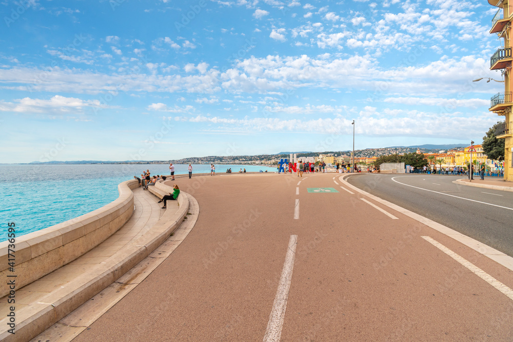 Tourists and locals enjoy the seaside pedestrian access at the Bay of Angels on the French Riviera in Nice France with the #Ilovenice sign in view.
