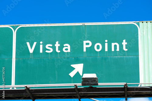 Vista Point road sign in green with a right pointing arrow showing drivers the direction to scenic overlook. Blue sky.