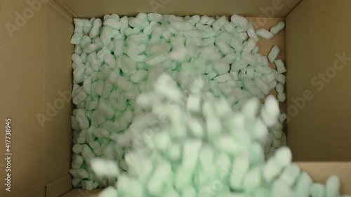 Storyfoam Packing peanuts being poured falling into cardboard box, care shipping products for customers by packaging starch protective granules . Online shopping retailer
