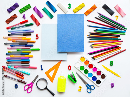 Bright still life scene of stationery on a white background. Colored pencils, felt-tip pens, plasticine and paints, flat lay with a place for text.