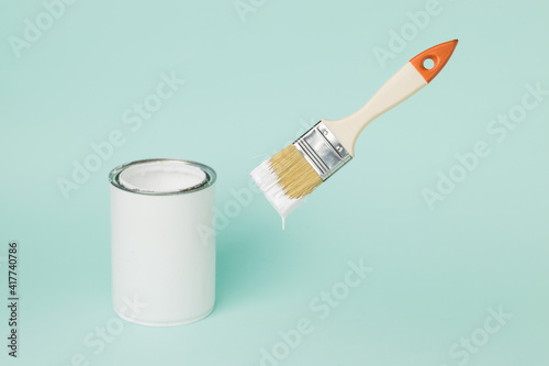 Fototapeta Naklejka Na Ścianę i Meble -  A jar of white paint and a levitating brush on a blue background.