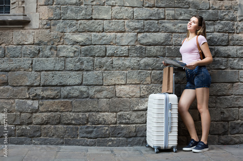 Smiling woman with travelling bag on stone wall background outdoors