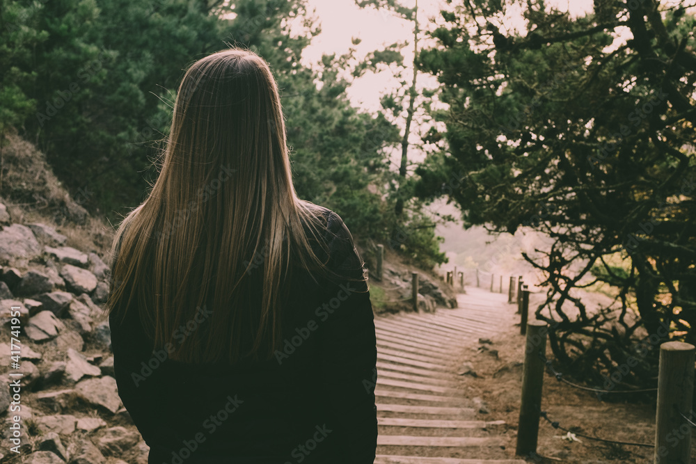 Behind the back of a woman in the woods during magic hour Behind the back of a woman in the woods during magic hour