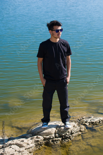 boy model standing at shore of lake wearing black t-shirt black pant and looking away