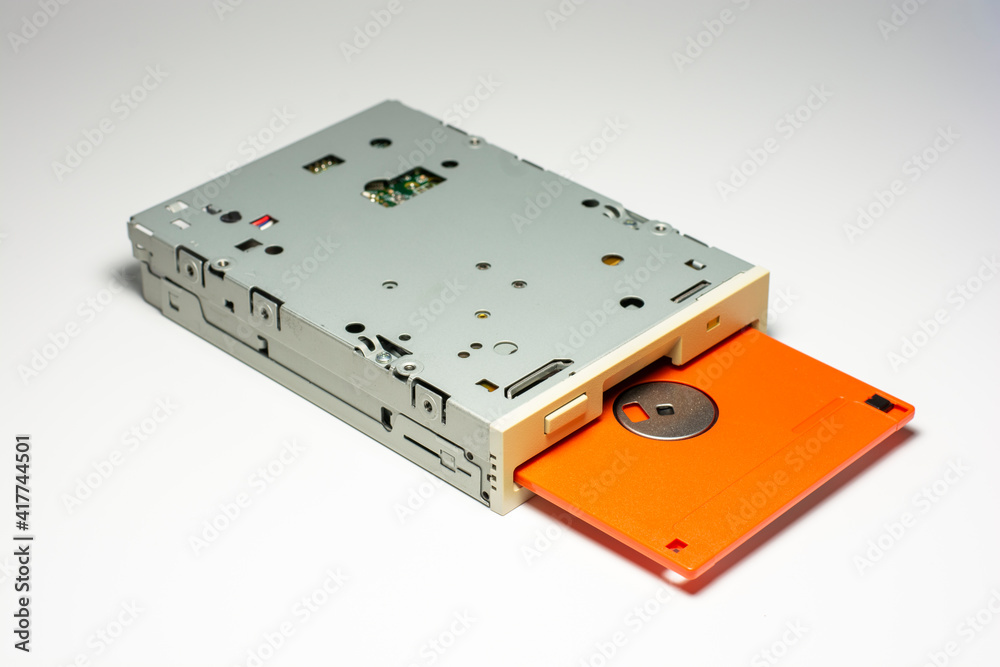 Floppy disk drive with orange diskette inserted isolated on white background.
Floppy disk drive with orange diskette inserted isolated on white background.