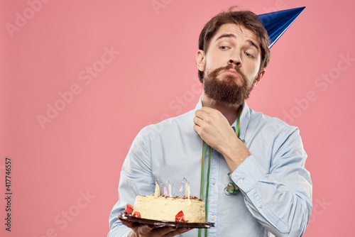 Bearded man with cake tongue on a pink background cropped view and a blue cap on his head