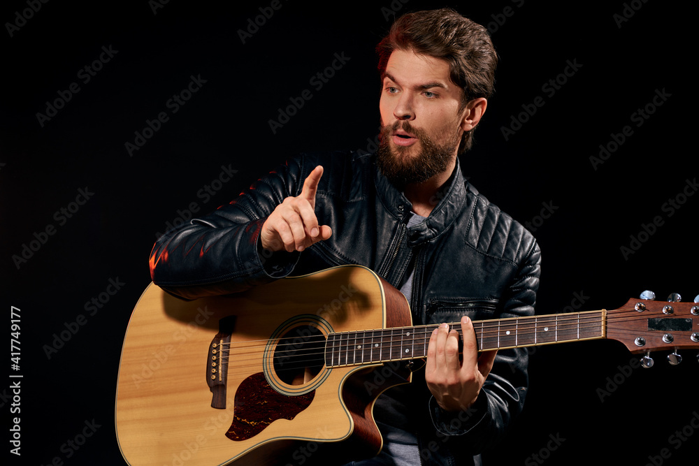 Fototapeta premium A man with a guitar in his hands leather jacket music performance rock star modern style dark background