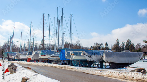 Sailboats line the perimeter of the Thornbury Yacht Club during the winter months when the harbor is frozen. The boats are winterized and covered up. The marina is frozen and the docks snowy. photo