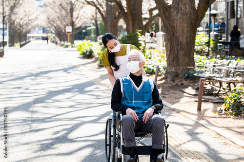 車椅子の高齢男性と介護福祉士の女性がマスクをして散歩している
