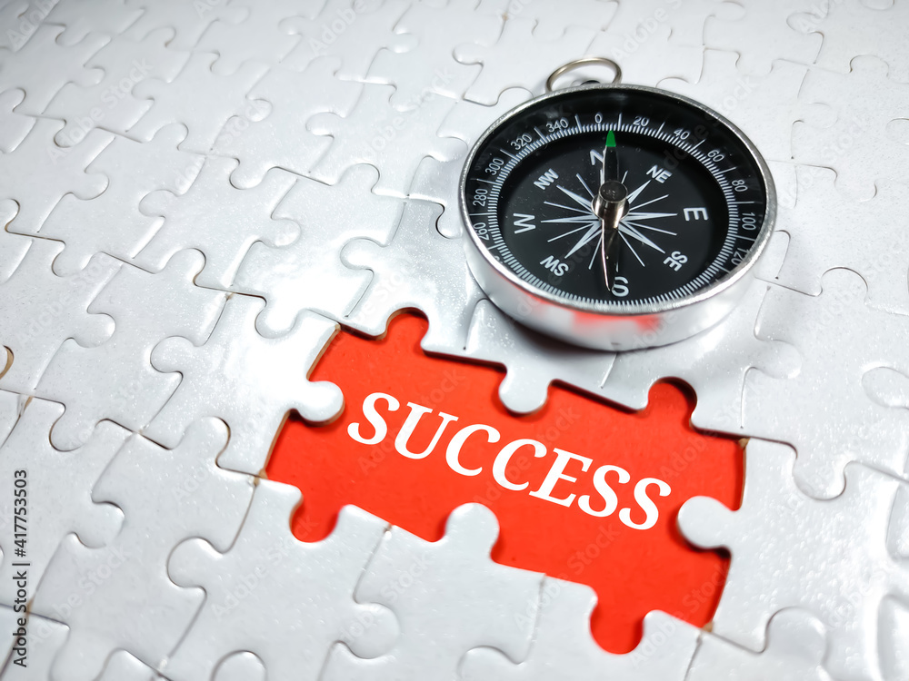 Selective focus.Word SUCCESS with compass on jigsaw puzzle and red background.Business concept. Selective focus.Word SUCCESS with compass on jigsaw puzzle and red background.Business concept.