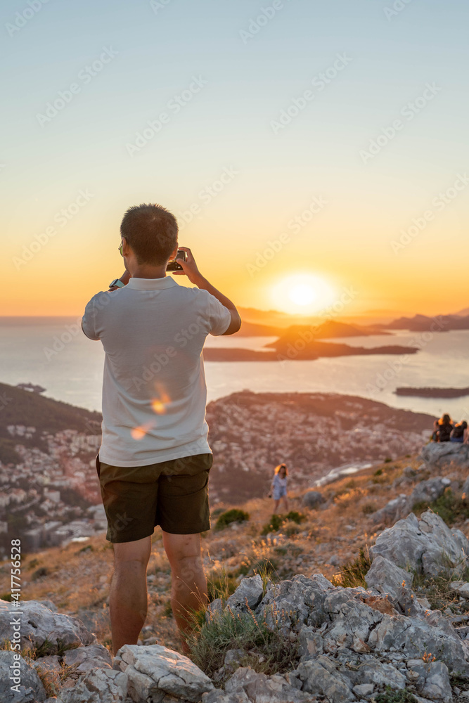 Tourist take photo of sunset over Dubrovnik old town Adriatic Islands coastline in summer from Mountain Srd
