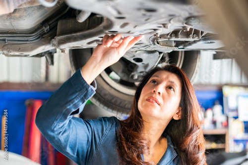 Asian woman mechanic working under vehicle in a car service. Empowering woman using wrench underneath the car.