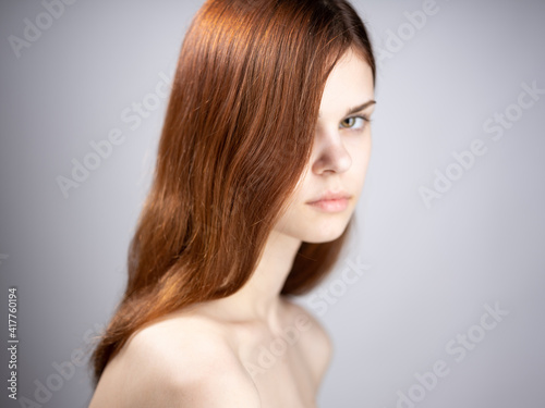 Portrait of a luxurious woman with red hair and bare shoulders on a gray background