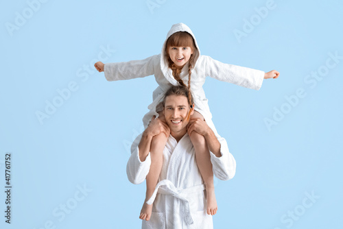 Portrait of happy father and daughter in bathrobes on color background