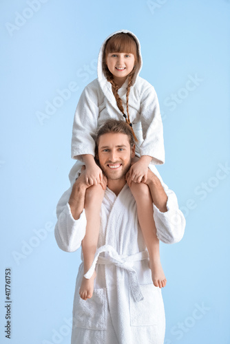 Portrait of happy father and daughter in bathrobes on color background