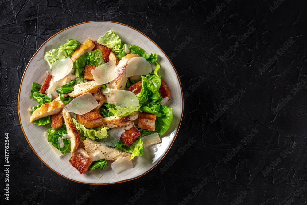 Caesar salad with chicken, shot from above with copy space on a black background Caesar salad with chicken, shot from above with copy space on a black background