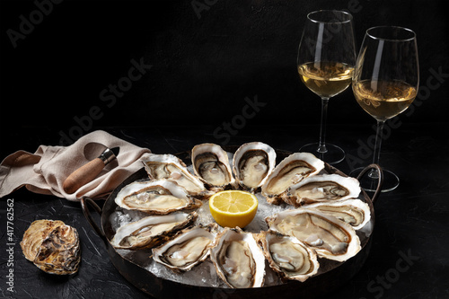 Oyster dozen with white wine and lemon, on a black background with copy space