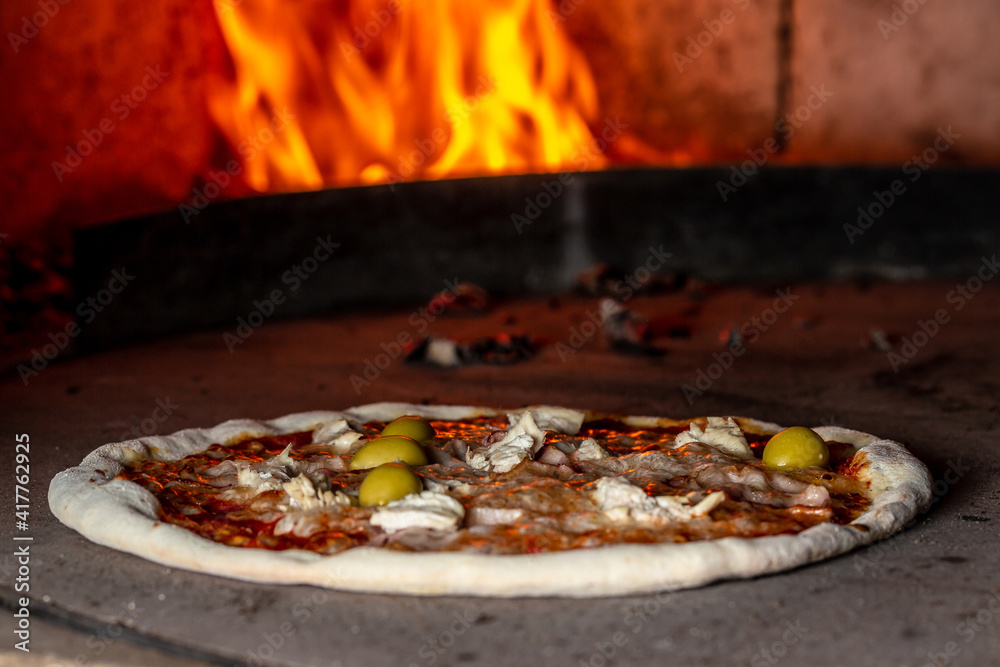 Pizza baking close up in the oven. Italian pizza is cooked in a wood-fired oven. Traditional baked wood fired oven