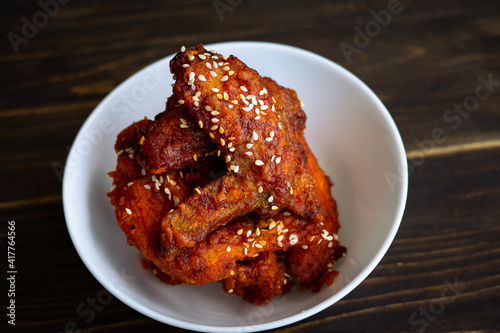 Chunks of fried chicken in a spicy sauce and sesame seeds. Food Korean cuisine on a wooden background.