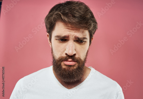 Sad man crying on a pink background in a white t-shirt cropped view