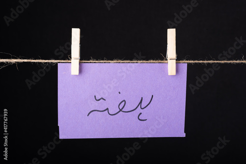 Translation Saturday in urdu word written on a Purple color sticky note hanging with a wire on black background