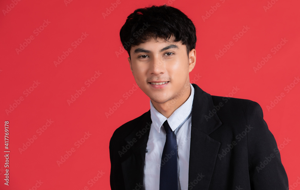 Portrait of young smart and handsome Asian male in blck suit posing with friendly face and self-confidence gesture on red background Portrait of young smart and handsome Asian male in blck suit posing with friendly face and self-confidence gesture on red background