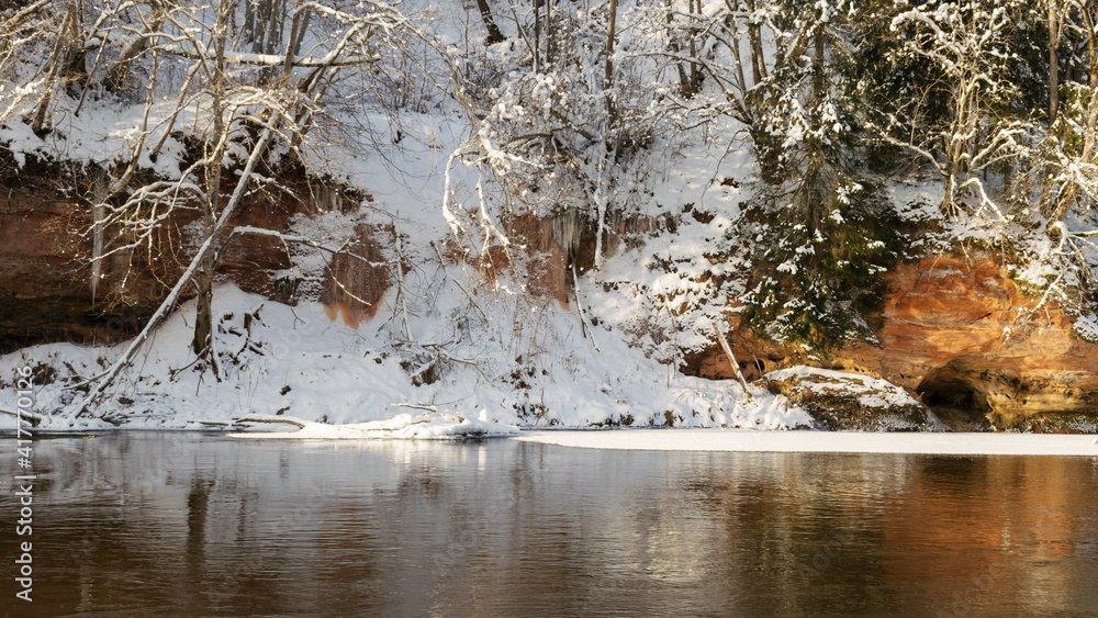 sunny day, landscape with red sandstone cliffs that are snowy with snow, frozen icicles on the cliff wall, icefall on the cliff wall, frozen river, Gauja, Kuku cliffs, Latvia sunny day, landscape with red sandstone cliffs that are snowy with snow, frozen icicles on the cliff wall, icefall on the cliff wall, frozen river, Gauja, Kuku cliffs, Latvia