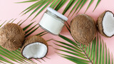 Jar of coconut oil and fresh coconuts with palm leaves on pink background top view.