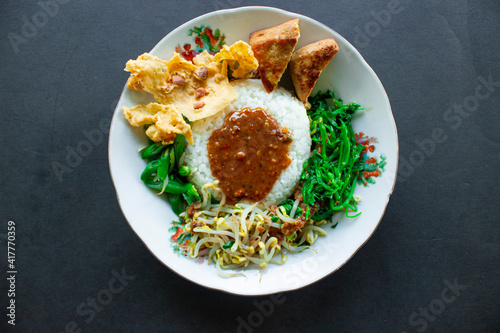 Nasi Pecel or sego pecel is Traditional Javanese rice dish of steamed rice with vegetable salad, peanut sauce, tempeh, tofu bean sprouts and crackers or peyek kacang. photo