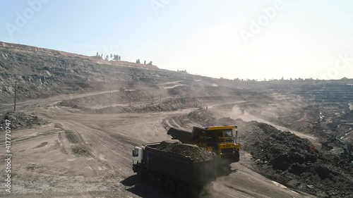 Aerial survey of truck. Dump truck carrying coal along in coal mine. Truck moving on dirt country road. Truck is driving along echnological road. Transportation of coal in trucks on road in open mine photo