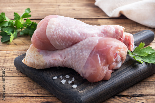 Raw chicken drumsticks with parsley and spices on a wooden cutting Board.