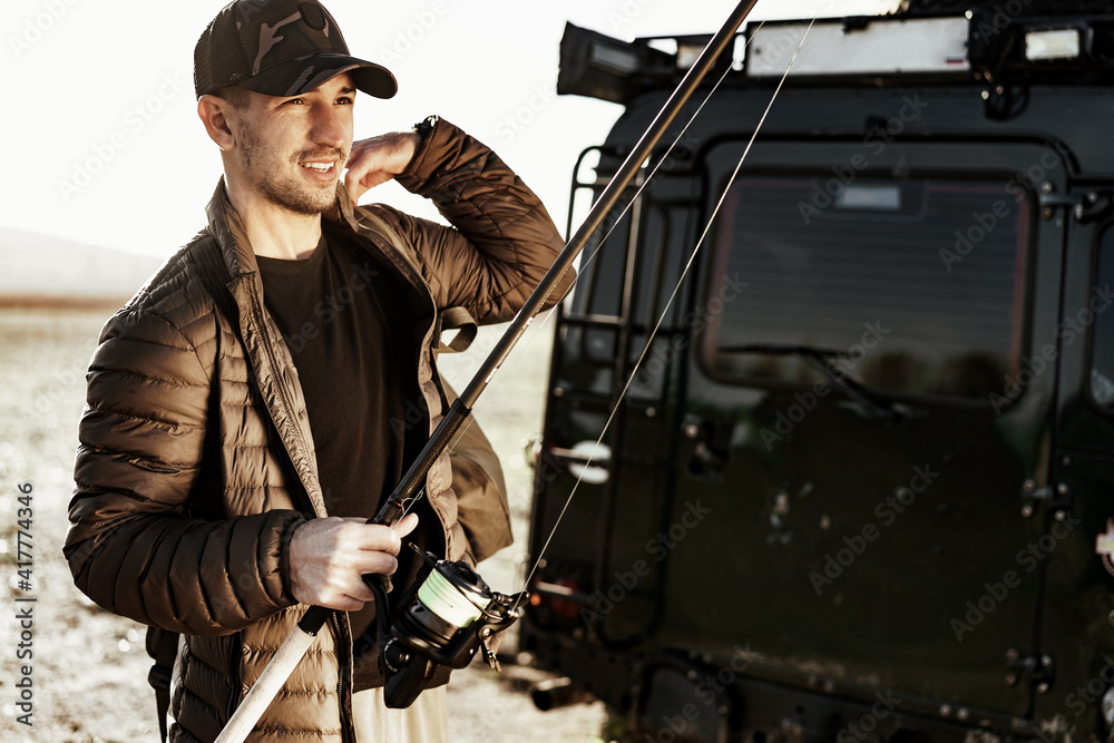Fototapeta premium Young fisherman standing near his car and holding fishing equipment