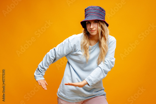 Stylish girl in panama hat dancing against yellow background