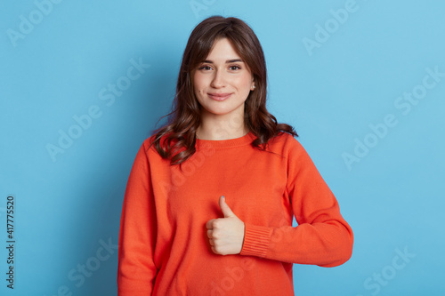 Canvas Print Image of beautiful brunette woman wearing casual clothes showing thumbs up and looking directly at camera at camera with cute charming smile, posing isolated over blue wall