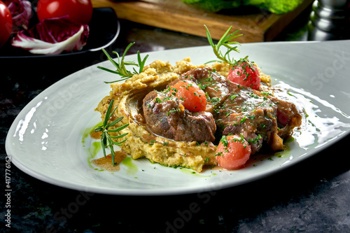 Close up view on Stewed Osso Buco steak with tomatoes, mashed potatoes served in a white plate on a dark marble background. Italian steak. Restaurant food