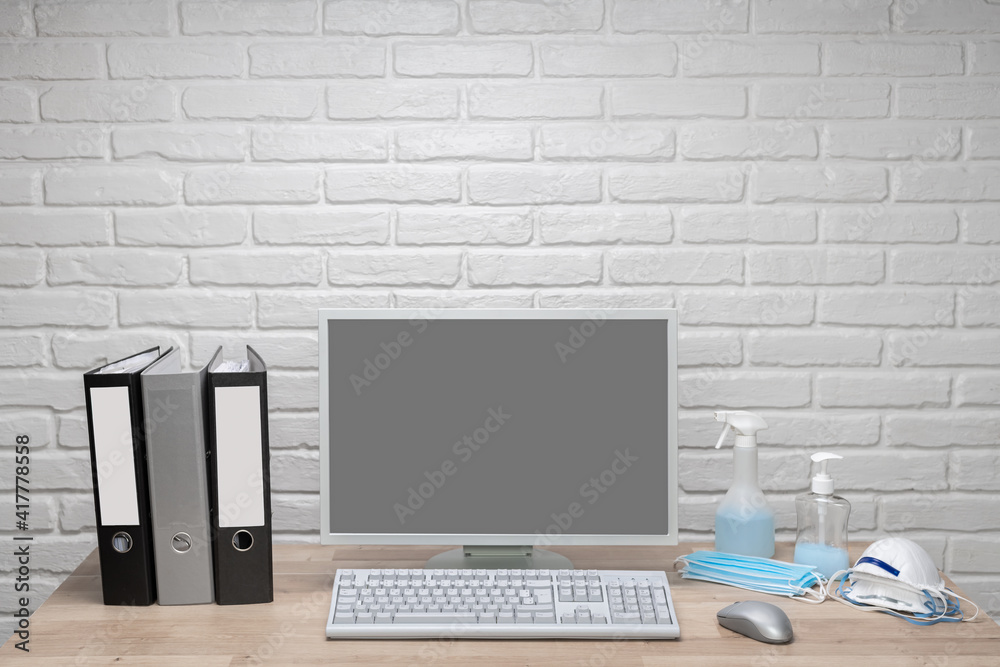 Fototapeta premium Blank screen computer monitor on working desk with folders, and corona protection