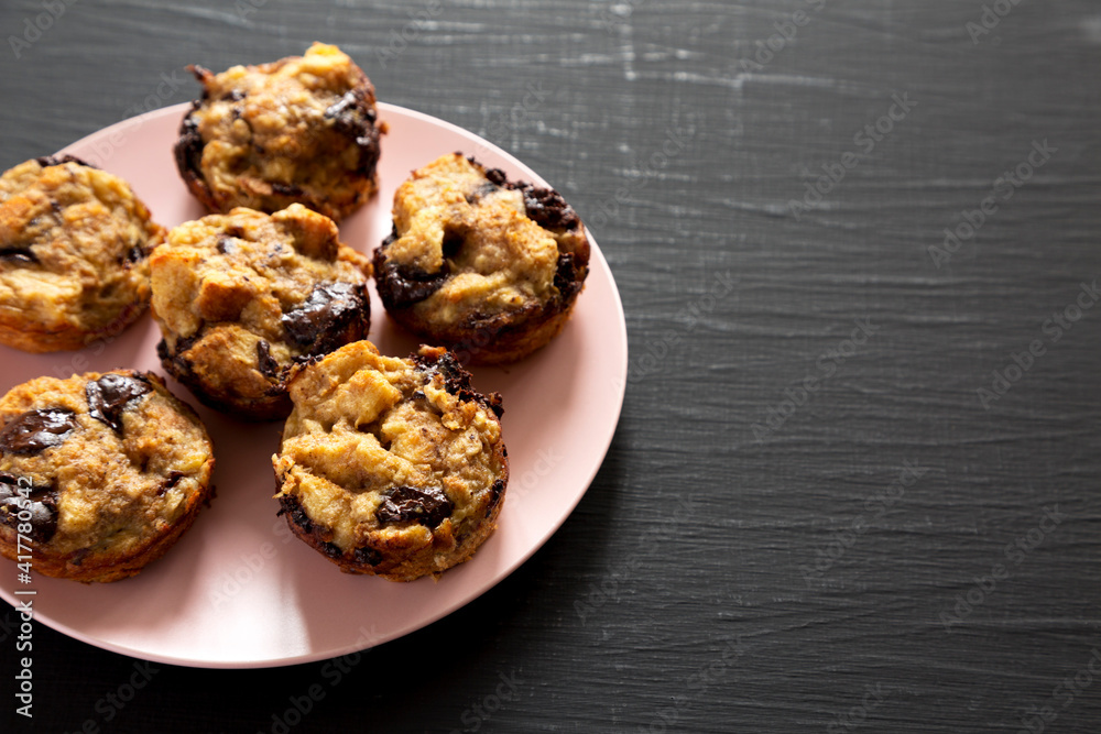 Homemade Chocolate Banana Bread Pudding on a pink plate on a black surface, side view. Copy space. Homemade Chocolate Banana Bread Pudding on a pink plate on a black surface, side view. Copy space.