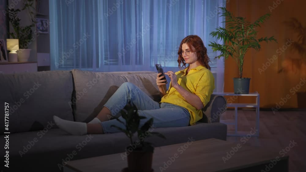cheerful woman with mobile phone in hands uses Internet while sitting resting at home on couch in evening shows finger up, has an idea cheerful woman with mobile phone in hands uses Internet while sitting resting at home on couch in evening shows finger up, has an idea