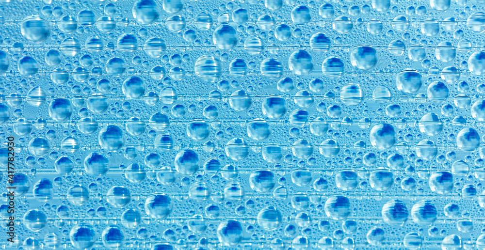 Water drops on blue glass as an abstract background.