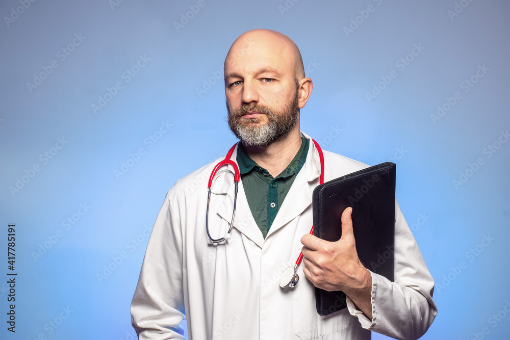 Bald doctor with beard on a blue background. The model is in his 40s. Looking at a open folder. Wearing white uniform. Holding black folder. Bald doctor with beard on a blue background. The model is in his 40s. Looking at a open folder. Wearing white uniform. Holding black folder.