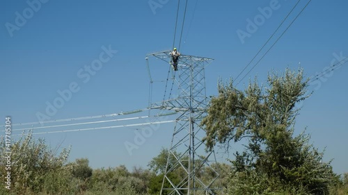Skilled worker installs aviation marker balls fastened to wires of power transmission lines above green trees low angle shot