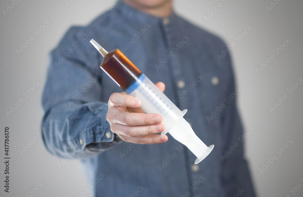 Man holds a large 160 ml syringe. Close up. Isolated on a gray background Man holds a large 160 ml syringe. Close up. Isolated on a gray background