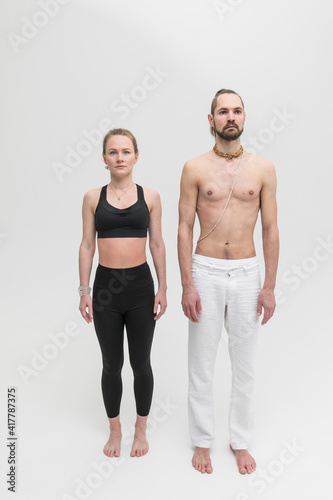 A man and a woman stand next to each other shoulder to shoulder before a yoga workout. Couple of young people in sportswear in studio on white background. © Artem Bruk